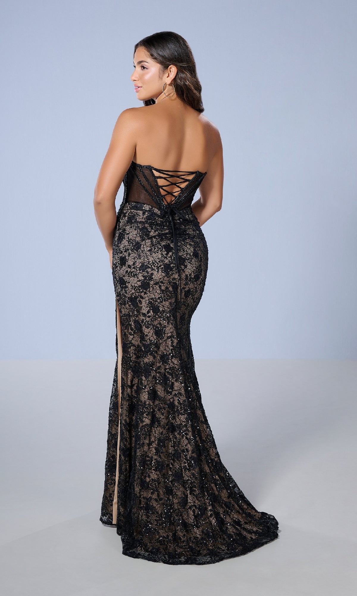 A woman models the Long Black Lace Prom Dress: Tiffany 16236, featuring a strapless design, sheer corset bodice, lace-up back, and side slit, posed against a plain light background.